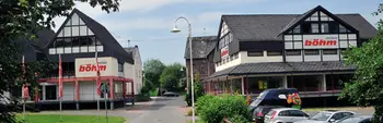 Blick auf das Möbelhaus Böhm in Dierdorf mit traditioneller Fachwerkarchitektur, zwei Gebäudeteilen und großem Firmenlogo, eingebettet in grüne Umgebung und mit angrenzendem Parkplatz.
